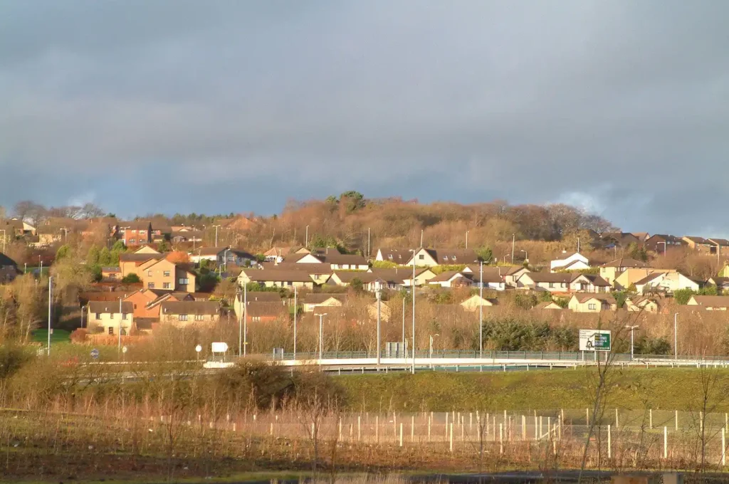 Residential housing locations in Cumbernauld, Scotland, viewed from a distance under a bright sky.